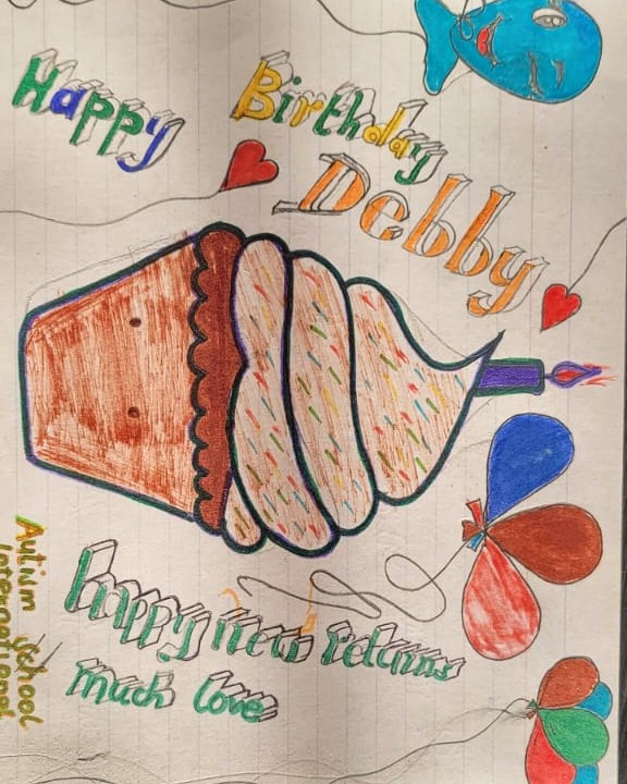 A hand-drawn birthday card with a cupcake, balloons and “Happy Birthday” lettering, made at Autism School International