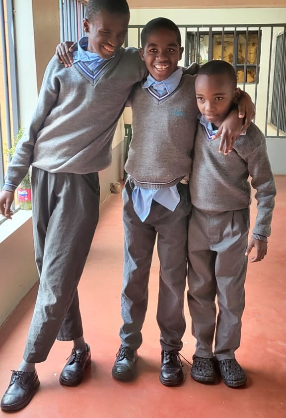 Three learners in school uniform standing together with their arms around each other
